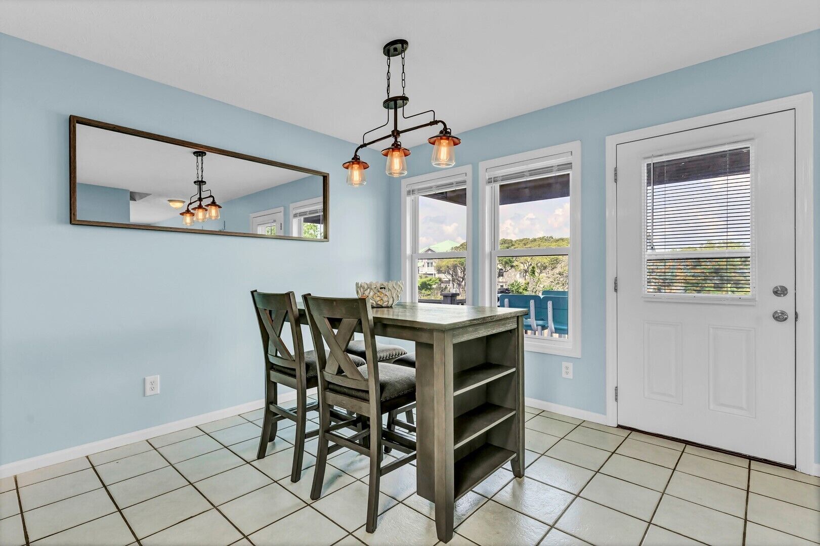A dining area with a table and chairs, a hanging light fixture, a large mirror, and a door with windows.