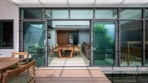 Une maison moderne dotée d’un coin repas, de grandes fenêtres en verre et d’une table en bois.