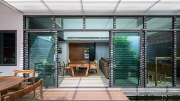 A modern house with a dining area, large glass windows, and a wooden table.