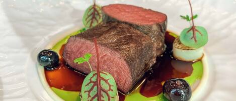 Un plato de comida con bistec, vegetales verdes y salsa.