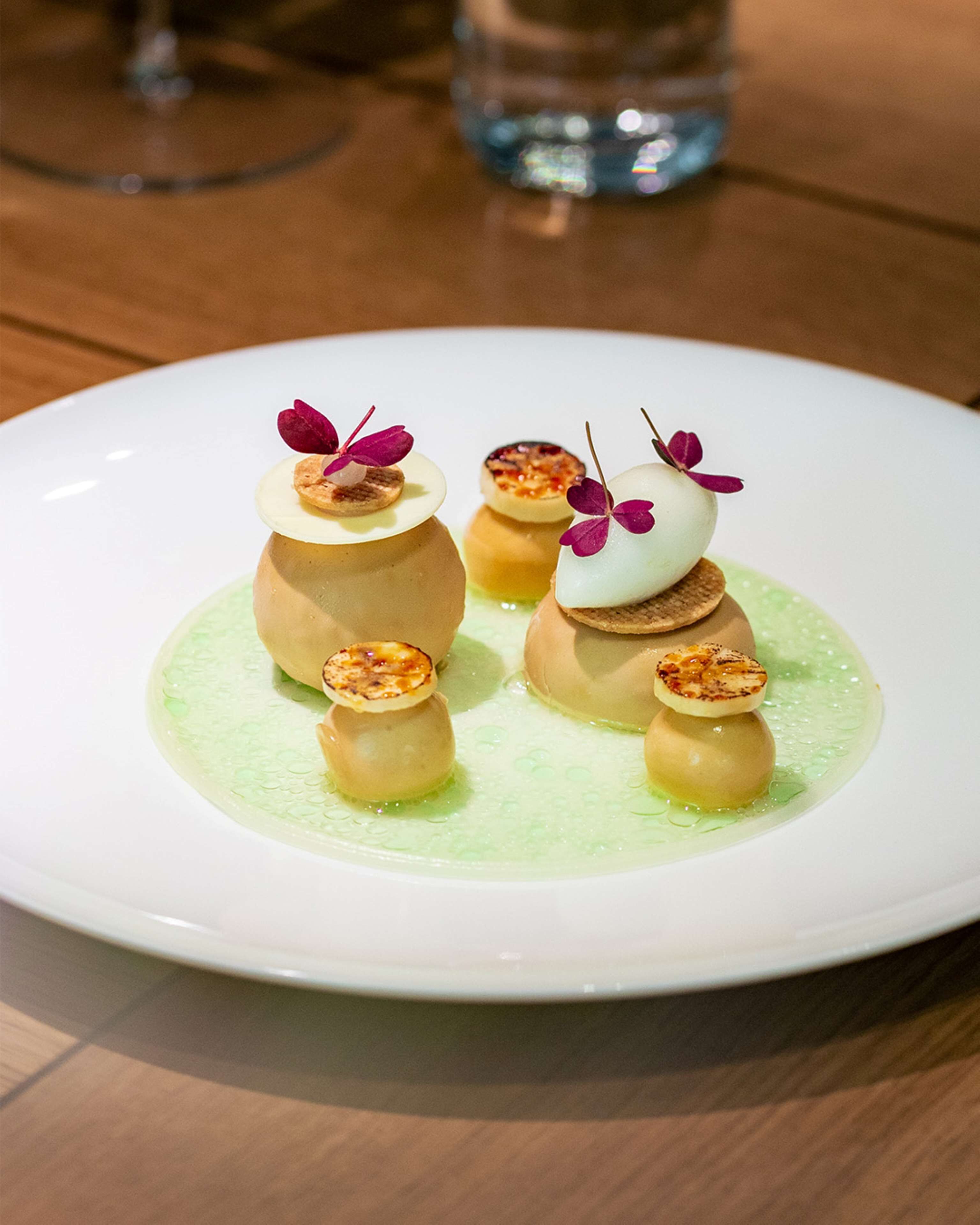 Un plato blanco con un postre que consiste en formas esféricas cubiertas con una flor y una fruta.