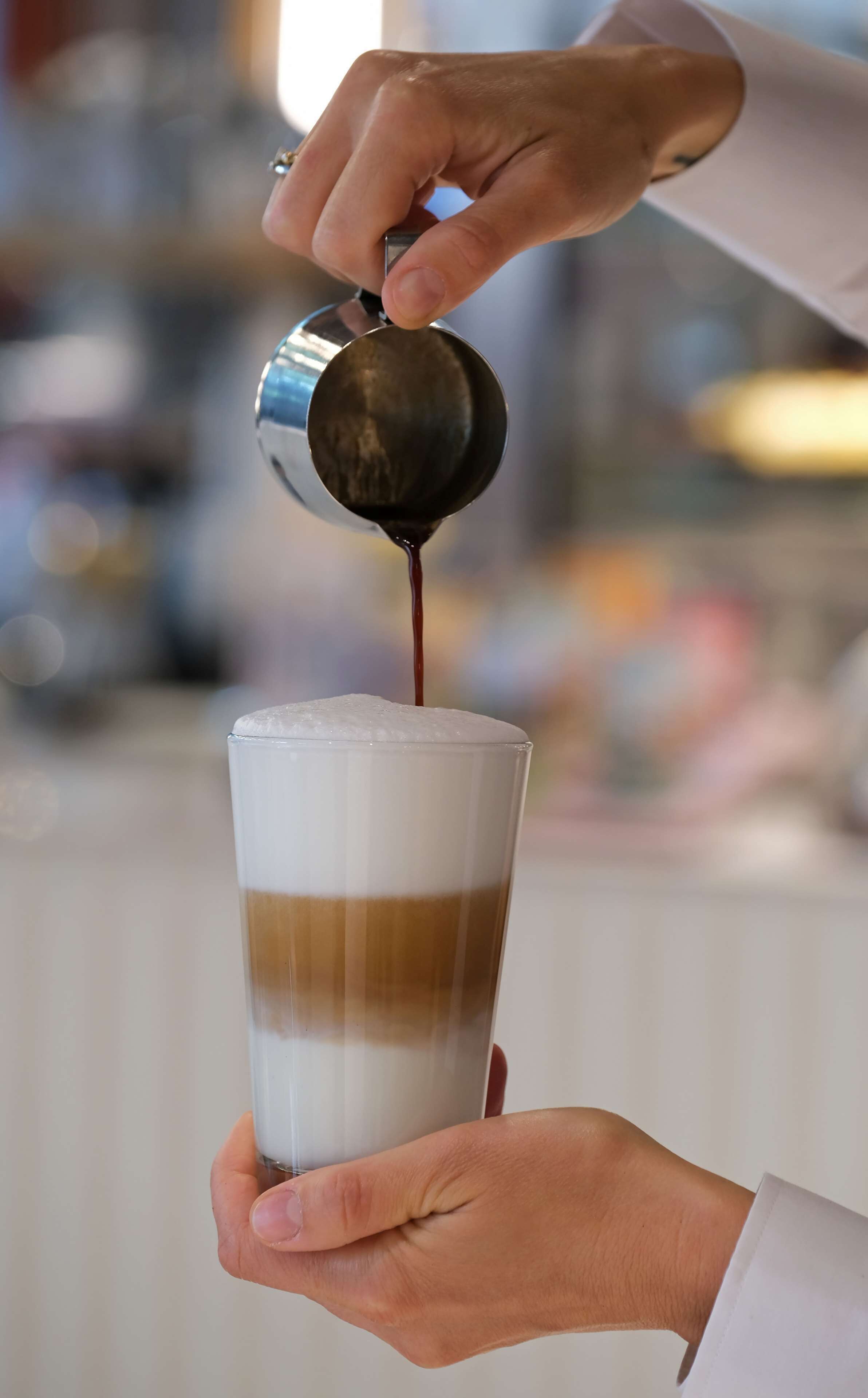 A person pouring a dark liquid into a glass with layers of different colors.