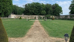 Ein Kiesweg führt zu einem Gebäude mit einer Steinmauer und Bäumen im Hintergrund.