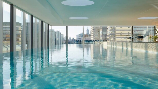 Piscina interior moderna com água cristalina, grandes janelas e vista para o horizonte urbano.