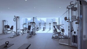 Uma academia com diversos equipamentos de exercício, um banco e vista para a cidade por grandes janelas.