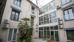 A building with multiple air conditioning units, a large potted plant, and a tiled patio area. - APPT 11 de la MAISON D'ANTONIN (Nîmes)
