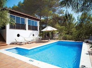 Ein Swimmingpool mit einem weißen Gebäude, Außenbereich zum Sitzen und Bäumen im Hintergrund.
