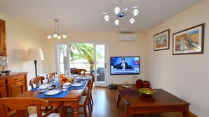 A dining area with a wooden table, chairs, a television, and a window with a view of palm trees. - Acogedor apartamento a 100 metros de la playa (Palmanova)