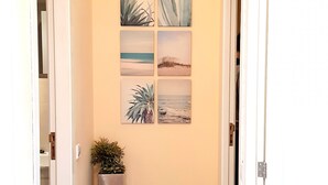 A hallway with a wooden floor, a potted plant, and four framed pictures on the wall. - Acogedor apartamento a 100 metros de la playa (Palmanova)