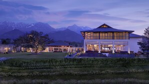 Un hotel moderno con un amplio frente de cristal, un área de estar al aire libre espaciosa y una vista de montañas nevadas al fondo.