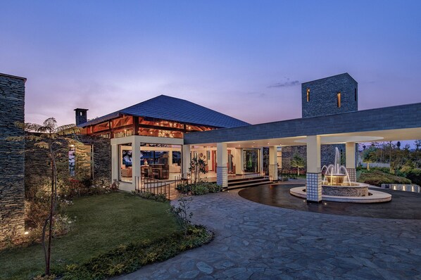 Una casa moderna con fachada de piedra, un patio amplio y una fuente.