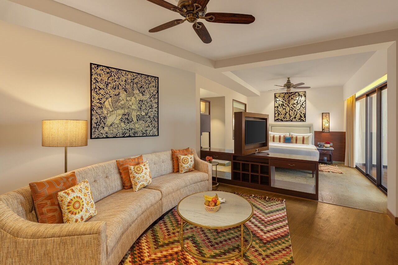 A modern hotel room with a sofa, a round coffee table, a TV, a bed, and a ceiling fan.