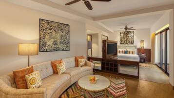 A modern hotel room with a sofa, a round coffee table, a TV, a bed, and a ceiling fan.