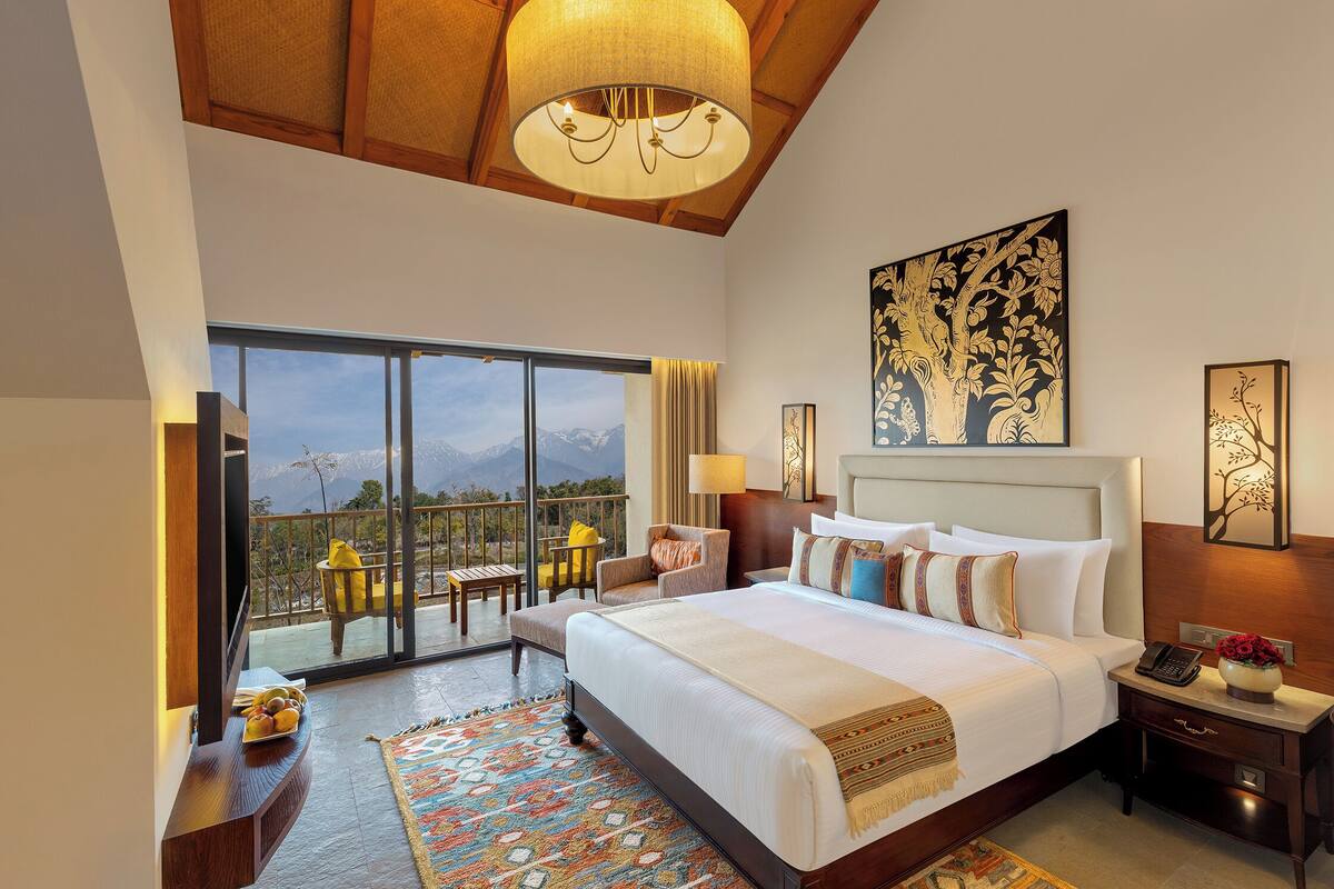 Um quarto espaçoso com uma cama grande, uma varanda com vista para as montanhas e um candelabro.