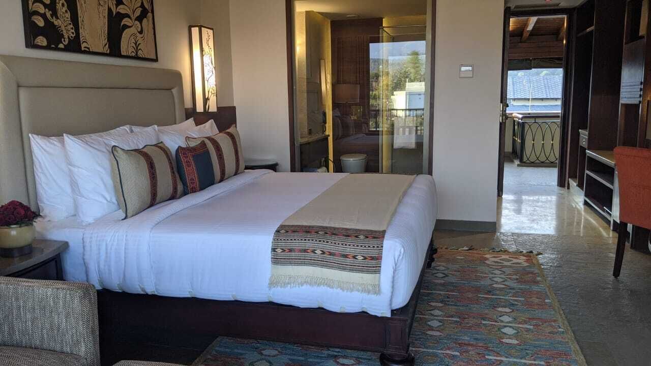 A hotel room with a large bed, a bedside table with a lamp, a chair, and a view of the balcony.