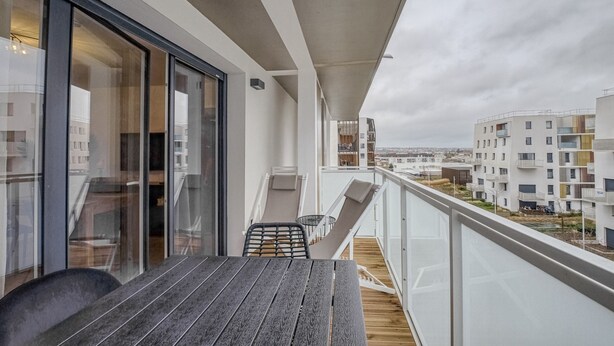 A balcony with a wooden table and chairs, a glass door, and a view of the cityscape.