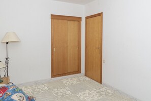 A bedroom with two wooden doors, a floor lamp, and a patterned rug. - VILLAS CAP BLANC II, PTA 11 (Cullera)