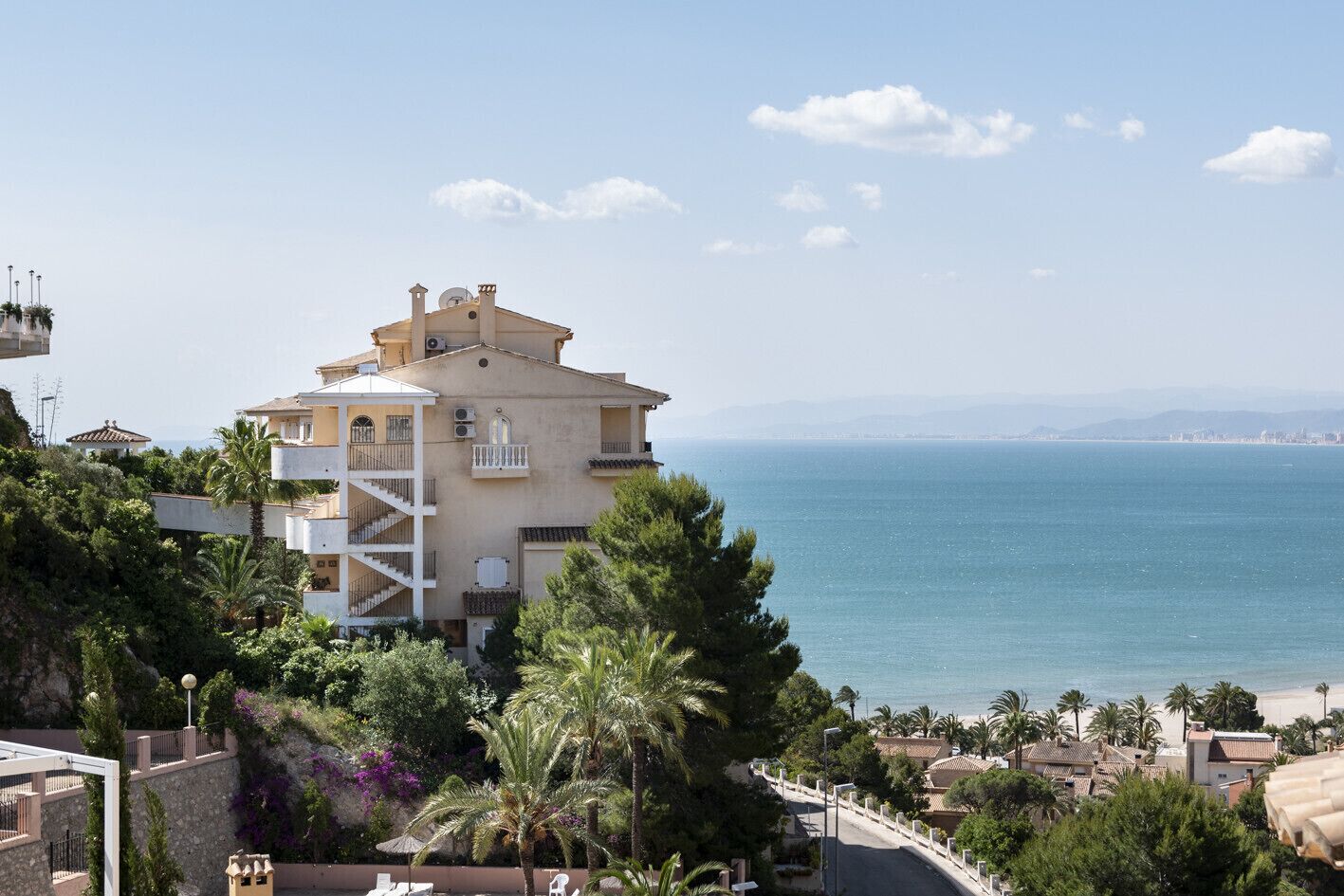 Un bâtiment situé sur la côte, doté d’un balcon, entouré de verdure et offrant une vue sur la mer.