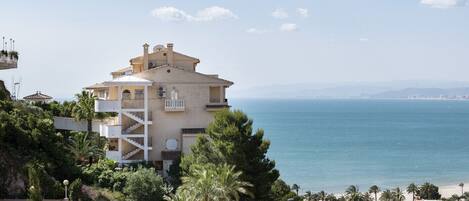 A coastal building with a balcony, surrounded by greenery and overlooking the sea.