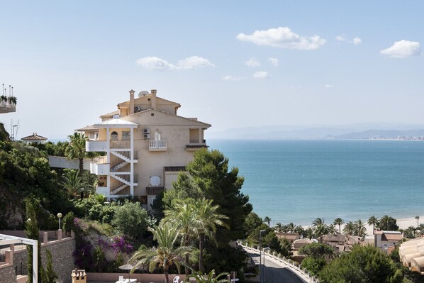 A coastal building with a balcony, surrounded by greenery and overlooking the sea.
