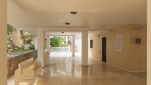 A spacious corridor with a tiled floor, white walls, and a view of greenery outside.