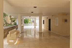 A spacious corridor with a tiled floor, white walls, and a view of greenery outside.