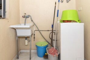 Baño pequeño con lavamanos, un cubo verde, un trapeador y un cubo para el trapeador.