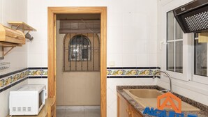 A compact kitchen with a wooden door, a window with metal bars, a microwave, and a sink with a countertop.