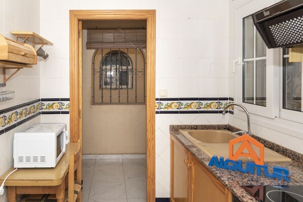 A compact kitchen with a wooden door, a window with metal bars, a microwave, and a sink with a countertop.