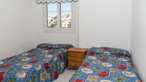 A bedroom with two single beds, a wooden dresser, and a window with a view of buildings.