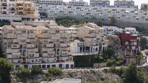 A densely packed residential area with multi-story buildings, balconies, and a rocky hillside.