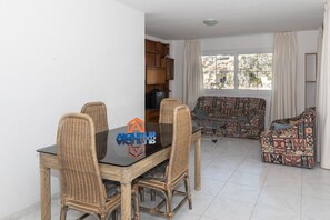 Una sala de estar con una mesa de comedor, sillas de mimbre, un sofá y un televisor.
