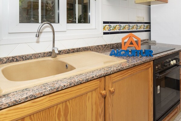 A kitchen with a granite countertop, a stainless steel sink, wooden cabinets, and a dishwasher.