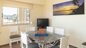 A dining area with a table, chairs, a television, and a painting of a sunset. - EL RACO, A-7º-13 (Cullera)