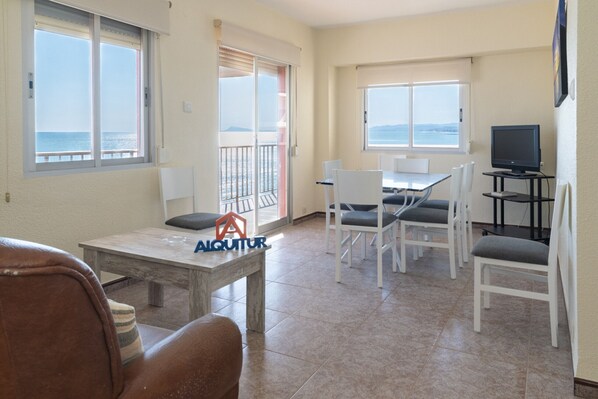 A room with a dining table, chairs, a sofa, a TV, and large windows with a view of the sea. - EL RACO, A-7º-13 (Cullera)