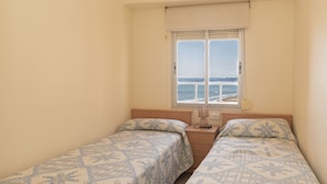 A bedroom with two beds, a window with a view of the sea, and a bedside table with a lamp. - EL RACO, A-7º-13 (Cullera)