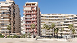 A multi-story hotel with balconies, palm trees, and a clear blue sky. - EL RACO, A-7º-13 (Cullera)