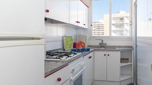 A compact kitchen with white cabinets, a gas stove, a built-in oven, and a window offering a view of buildings. - EL RACO, B-8º-15 (Cullera)