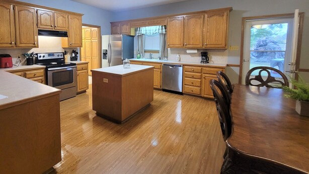 A kitchen with wooden cabinets, stainless steel appliances, a central island, and a dining table with chairs. - Newly Remodeled, Family Home, Near Interstate (Sulphur)