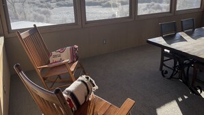 A room with a large window overlooking a snowy landscape. There is a wooden chair with a blanket, a table, and chairs. - 20+ Acres of Peace @ The Saratoga Hoemstead (Encampment)