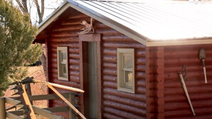 A log cabin with two windows and a door, a wooden staircase, and a shovel leaning against the wall. - 20+ Acres of Peace @ The Saratoga Hoemstead (Encampment)