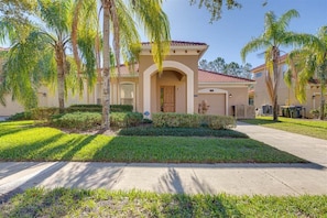 A residential house with a front entrance, a driveway, and palm trees.