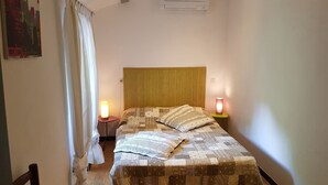 A bedroom with a bed, two bedside lamps, a window with curtains, and a wall-mounted air conditioner. - Gîte clim garage, Les Vans Ardèche, large panoramic terrace, gorges Ardèche (Les Assions)