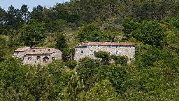 A stone building with a tiled roof, surrounded by dense greenery and trees. - Gîte clim garage, Les Vans Ardèche, large panoramic terrace, gorges Ardèche (Les Assions)