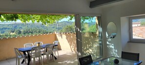 A balcony with a table and chairs, a sliding glass door, and a view of a forested hillside.