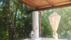 Un espace extérieur abrité, doté d’une structure blanche, d’un luminaire suspendu et d’une végétation luxuriante en arrière-plan.