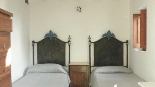 Une chambre avec deux lits simples, des têtes de lit en bois, une petite table de chevet et une armoire en bois.