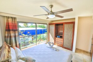Ein Hotelzimmer mit Bett, Deckenventilator, großem Fenster mit Vorhängen und Blick ins Freie.