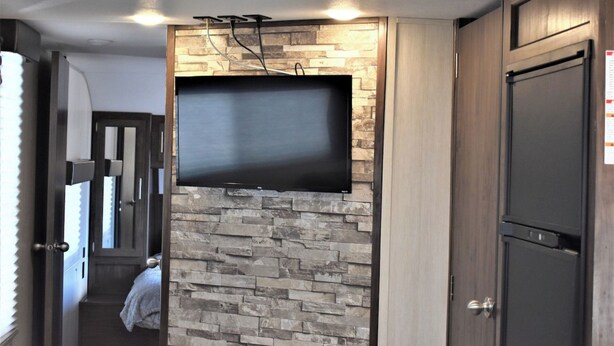 Un intérieur moderne avec un téléviseur fixé au mur en pierre, des meubles en bois et une porte dotée d’une poignée.