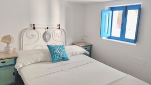 Une chambre avec un lit blanc, une fenêtre bleue et un mur blanc.
